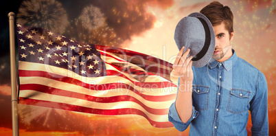 Composite image of portrait of hipster holding hat in front of f