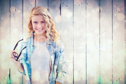 Composite image of smiling woman holding eyeglasses at desk