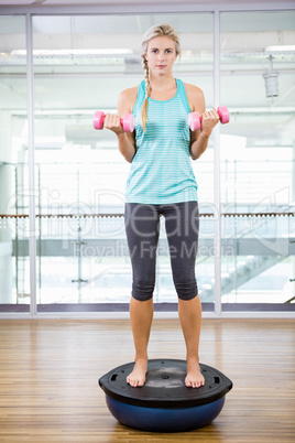 Fit blonde standing on bosu ball and lifting dumbbells
