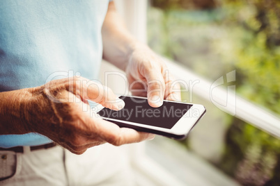 Senior man next to the window using smartphone