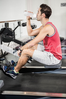 Muscular man on rowing machine drinking water