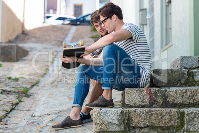 Hip men sitting on steps and holding skateboard