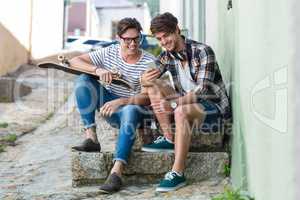 Hip men sitting on steps and looking at smartphone