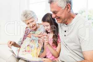 Happy grandparents with granddaughter reading a book