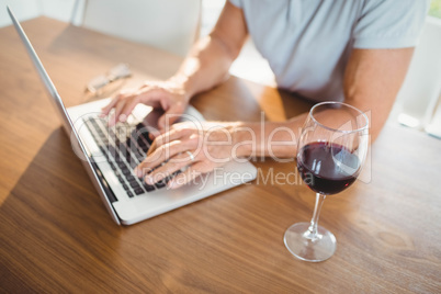 Focused senior man using laptop and drinking wine