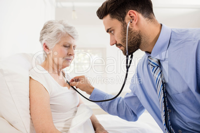 Home nurse listening to chest of patient with stethoscope