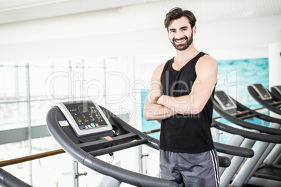 Smiling man standing on treadmill with arms crossed