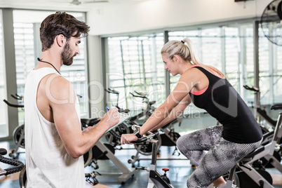 Trainer writing on clipboard and woman using exercise bike