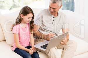 Smiling grandfather and granddaughter using laptop