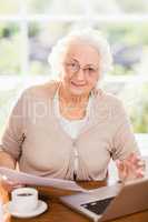 Senior woman dealing with documents while using laptop