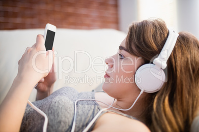 Pretty woman lying on the couch using her phone and listening mu