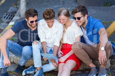 Hip friends looking at tablet and sitting on sidewalk
