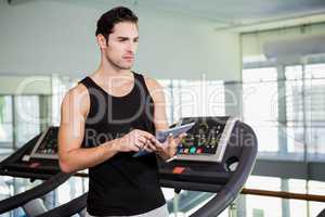 Serious man on treadmill standing with tablet