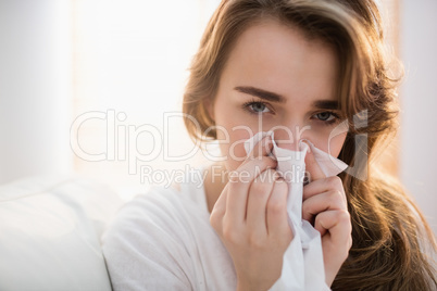 Woman blowing her nose on couch