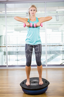 Fit blonde standing on bosu ball and lifting dumbbells