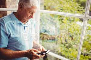 Senior man next to the window using smartphone