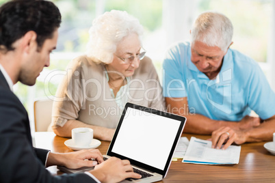 Businessman using laptop while senior couple is reading document