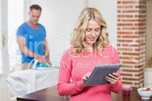 Woman using tablet while husband using iron