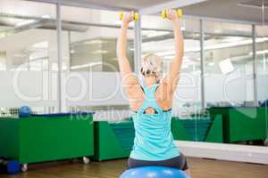 Fit woman lifting dumbbells and sitting on exercise ball