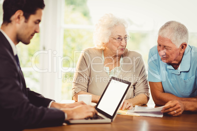 Businessman using laptop while senior couple is reading document