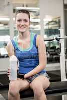 Smiling brunette on bench holding bottle of water