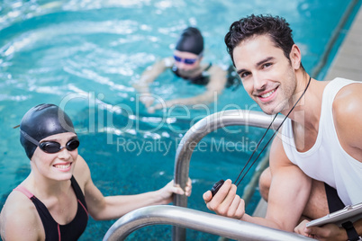 Smiling trainer showing stopwatch at swimmer