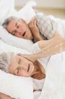 Awake senior woman in bed covering her ears