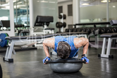 Muscular man doing push up with bosu ball