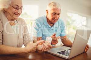 Senior couple using laptop and holding pills