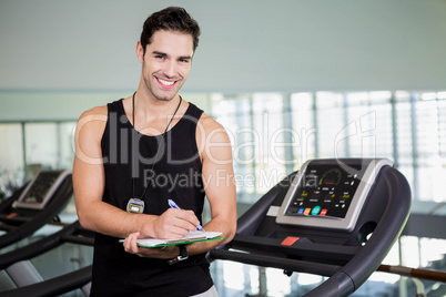 Smiling man on treadmill writing on clipboard