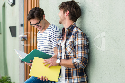 Hip men leaning against wall and holding notebooks