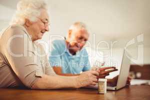 Senior couple using laptop and holding pills