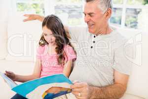 Smiling grandfather and granddaughter reading book