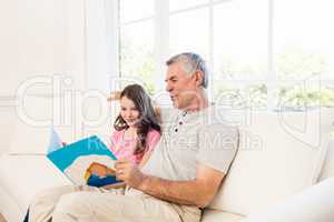 Smiling grandfather and granddaughter reading book