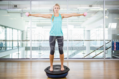 Fit blonde standing on bosu ball and lifting dumbbells