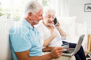 Smiling senior couple using laptop and smartphone