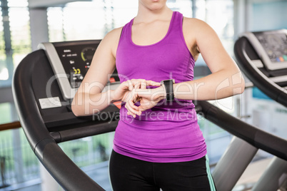Mid section of fit woman using smartwatch on treadmill