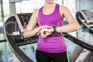 Mid section of fit woman using smartwatch on treadmill