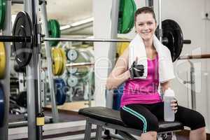 Smiling woman sitting on barbell bench and showing thumb up