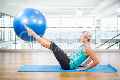 Fit blonde on mat holding with legs fitness ball