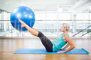 Fit blonde on mat holding with legs fitness ball