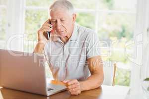Concentrated senior man looking at laptop and phone calling