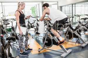 Female trainer looking at stopwatch and man using exercise bike