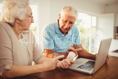 Senior couple using laptop and holding pills