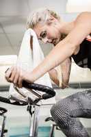Fit woman on exercise bike wiping sweat with towel