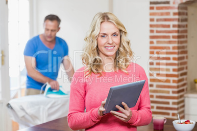 Woman using tablet while husband using iron