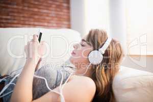 Pretty woman lying on the couch using her phone and listening mu