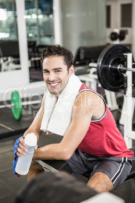 Smiling man sitting on bench and holding bottle of water