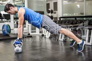 Muscular man doing push ups with kettlebells