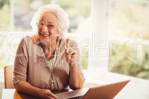 Smiling senior woman raising finger using laptop